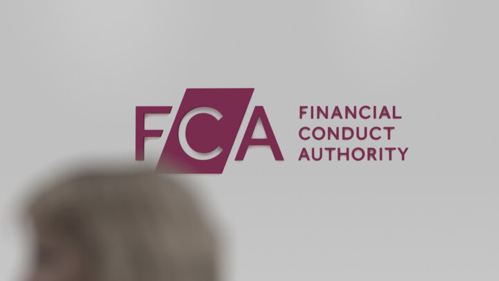 The logo of FCA Financial Conduct Authority on a white wall, in the foreground a blurry passerby.